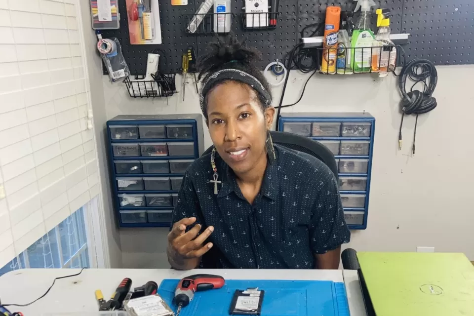 A Black woman works in a shop to prepare electronics for recycling..